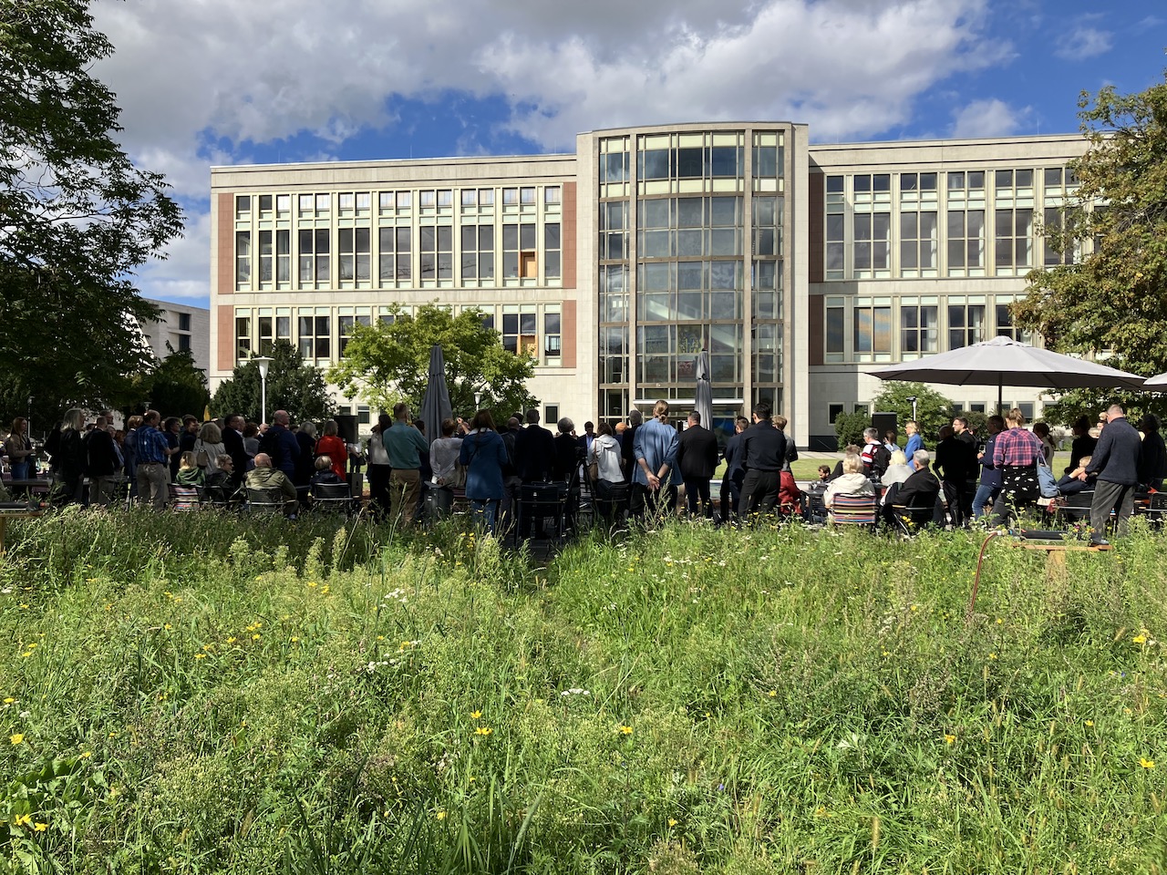 Menschen stehen in einem Garten. Im Hintergrund ein Gebäude.