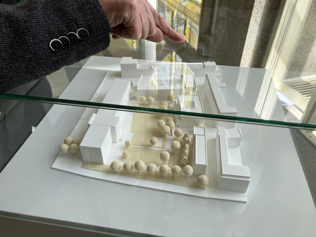 Hand zeigt mit Finger auf einen Glaskasten. Darin befindet sich ein Stadtmodell.