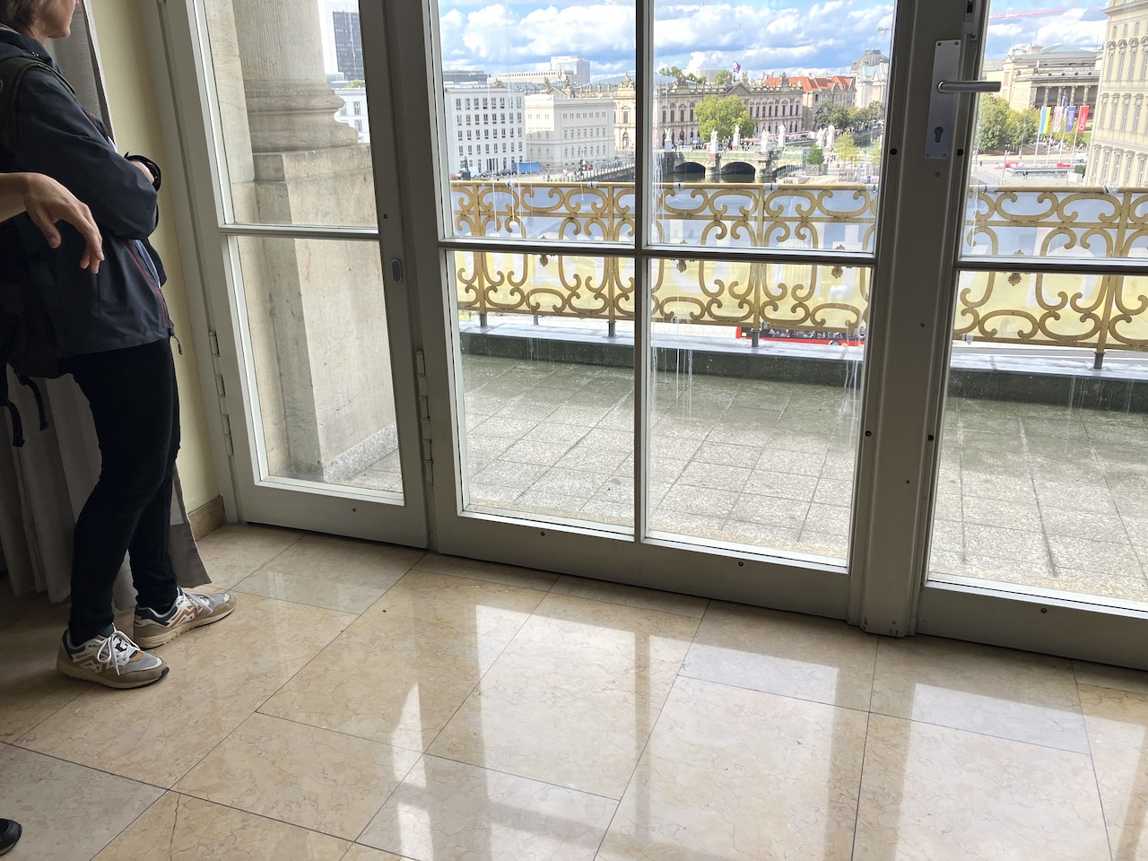 Blick von einem Gebäude auf einen Balkon hinaus in die Stadt: Geländer am Balkon, Brücke im Hintergrund, Gebäude