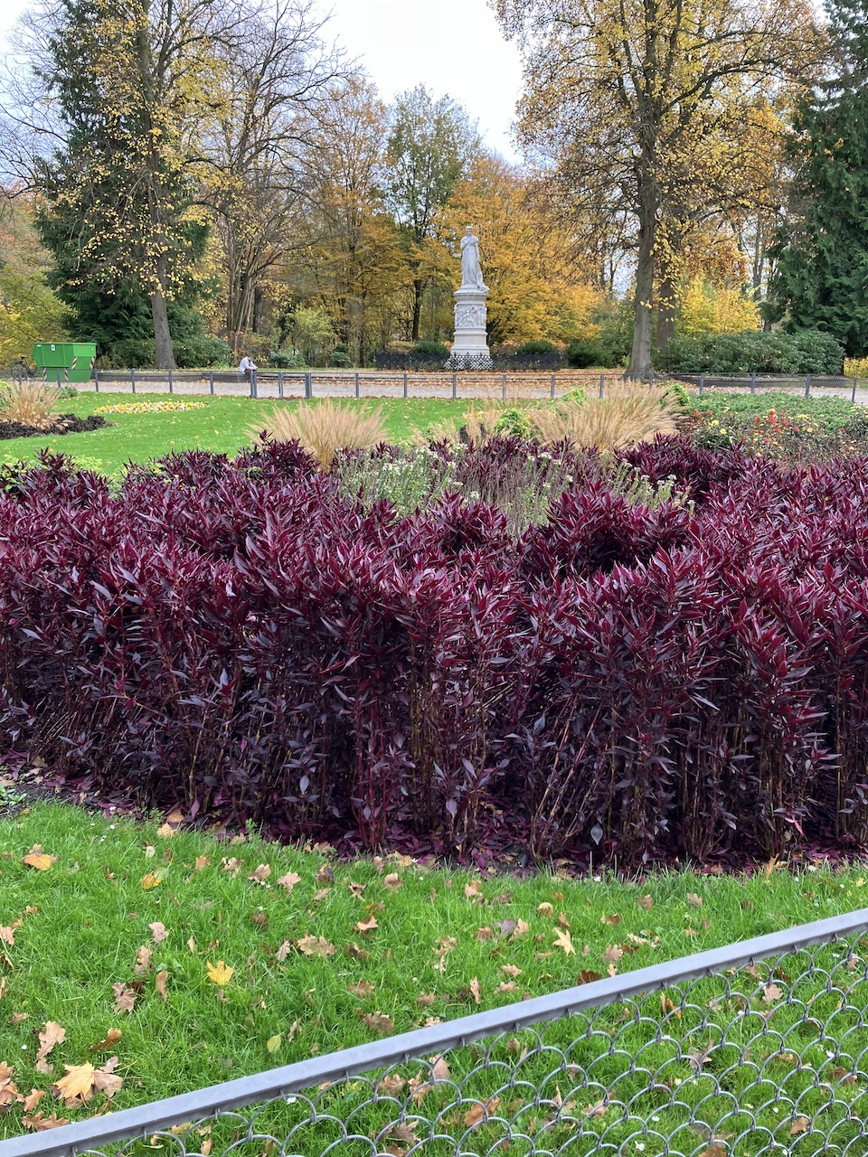 Blumenstauden in einem Park mit Denkmal und einem Zaun.